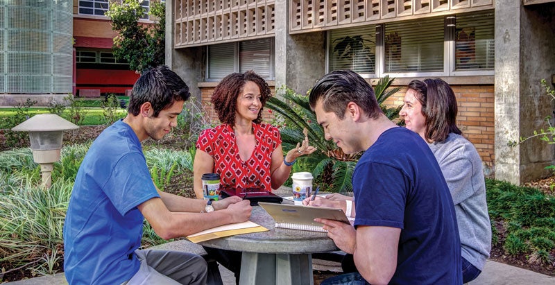 Two male students and two students sit at a small table with books and paper. 