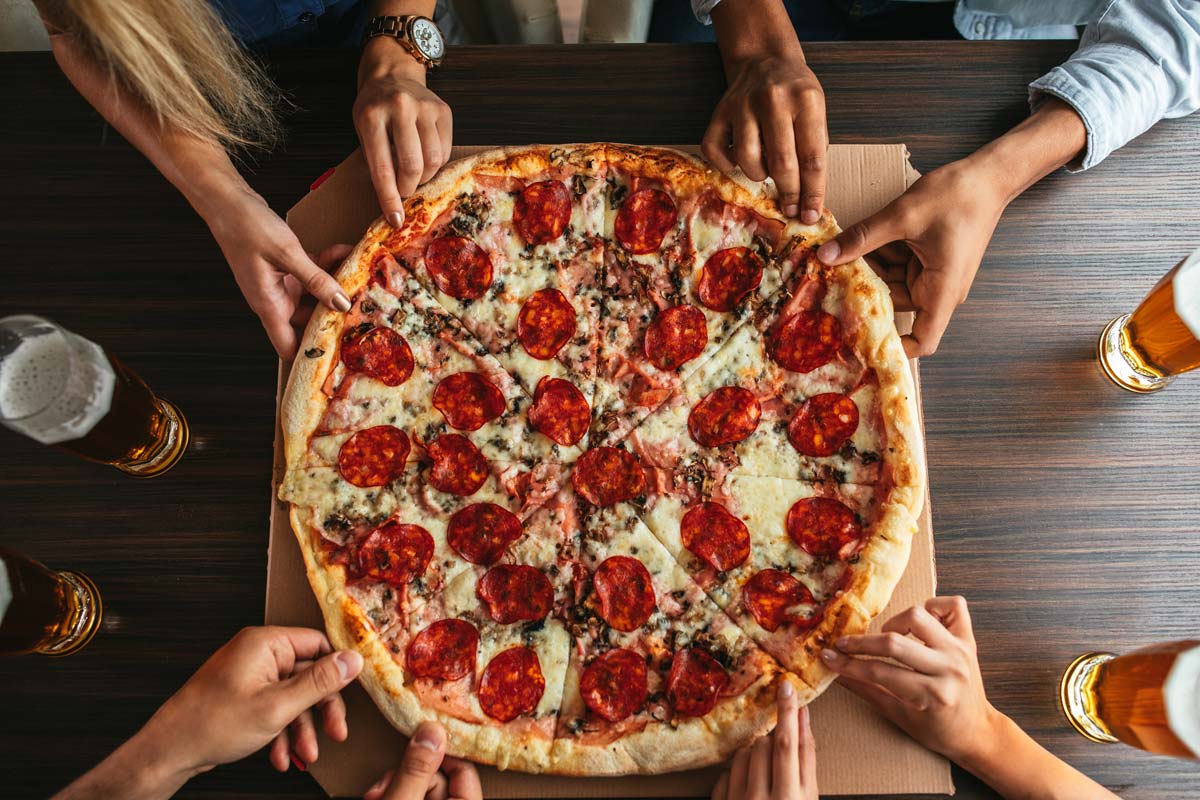 Aerial view of cheesy pepperoni pizza being shared by group of friends.