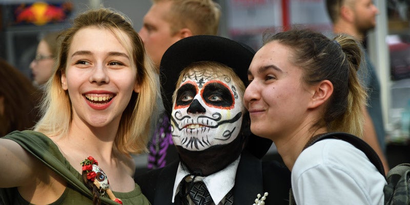 Three students celebrating Dia de los Muertos in downtown Riverside by taking a selfie with a face-painted friend.