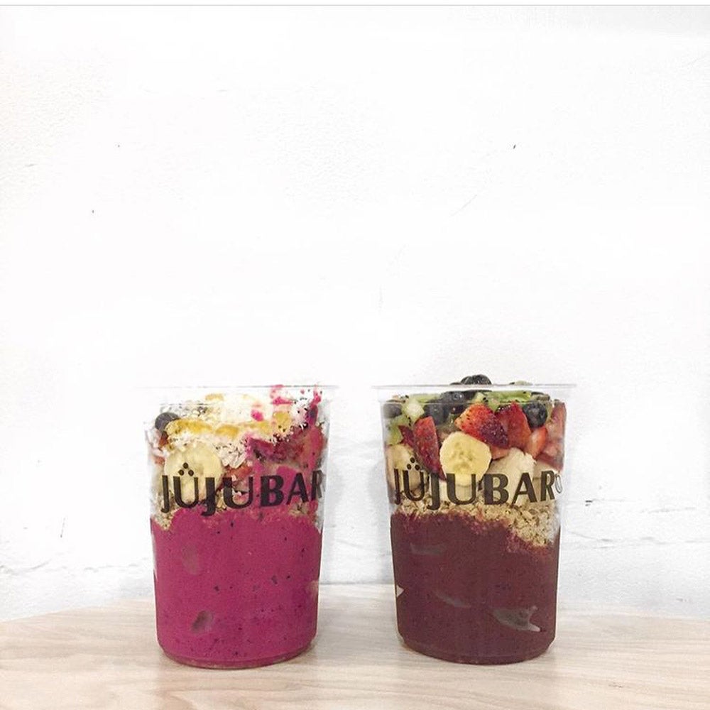 Two fruit smoothie cups with sliced assorted fruit and nutty toppings.  