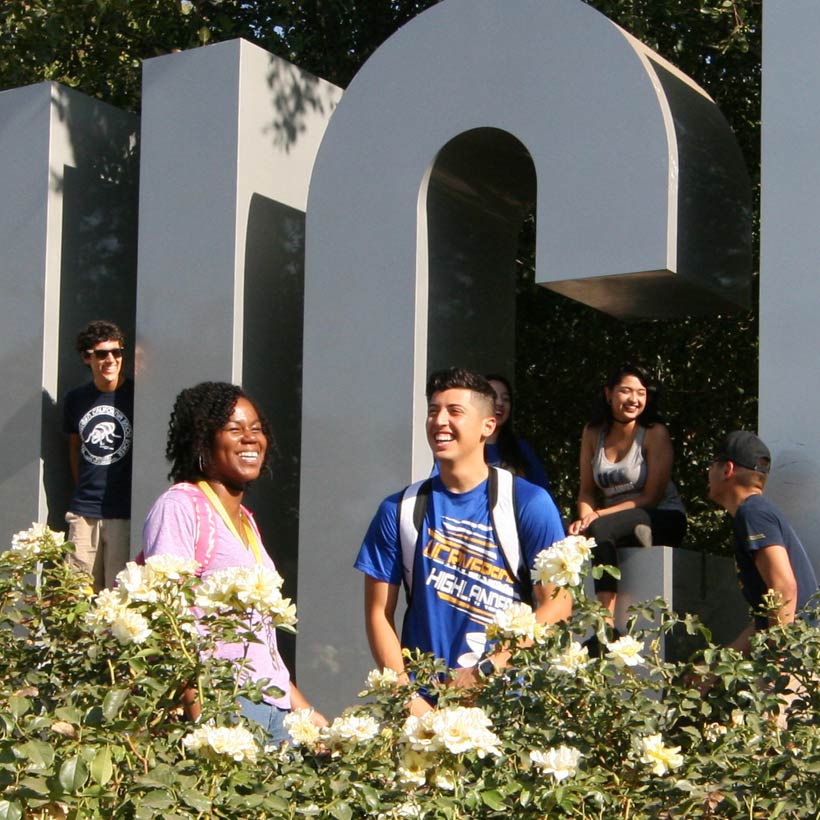 Several students share a laugh among blooming rose bushes on the UCR campus