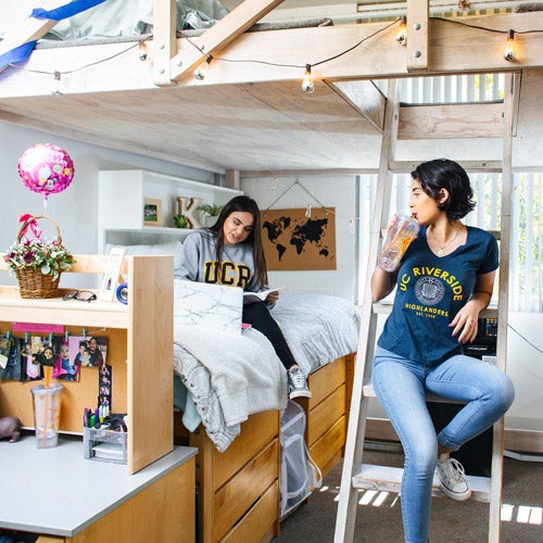 Two students, wearing their UCR gear, hang out inside a Housing Residence Hall room on campus.