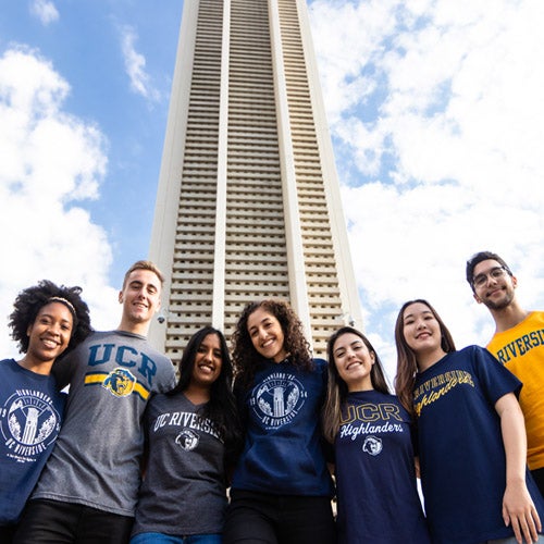 Seven students, representing the diversity of UCR's student body, stand shoulder to shoulder in front of the iconic bell tower on campus.