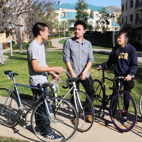 Three UCR students with bicycles take a moment to chat in front of the Residence Halls.