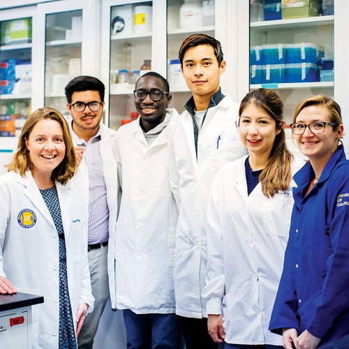 Six medical students stand together in their lab coats to smile for the camera.
