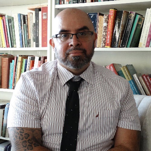 Alfonso Gonzales Toribio, associate professor in UCR's Department of Ethnic Studies, sits in front of a shelf of books.