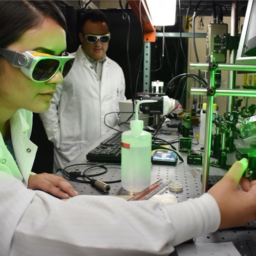 A UCR engineering student works in a lab while a professor offers instruction.