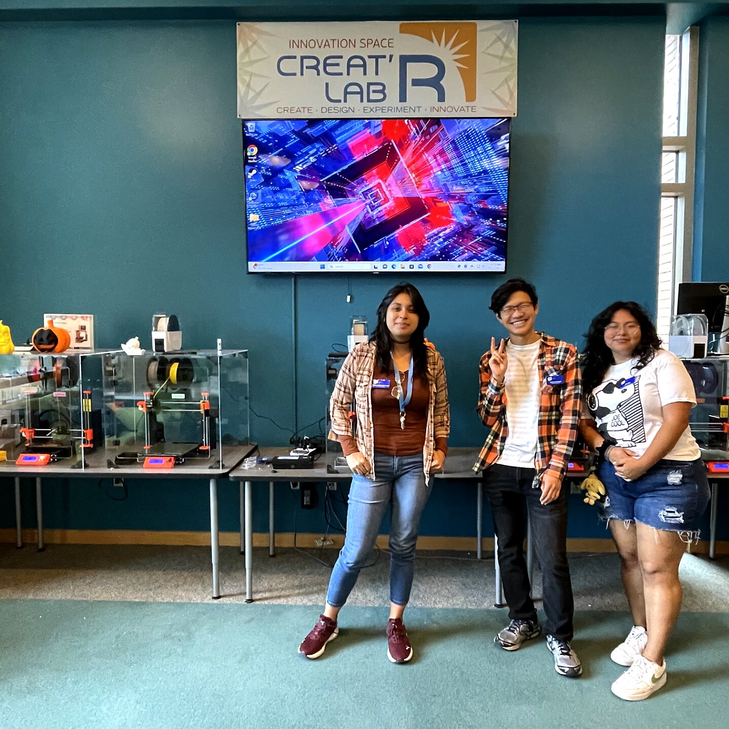 Three students, two females flanking one male, pose inside the Creat'R Lab on the UCR campus.