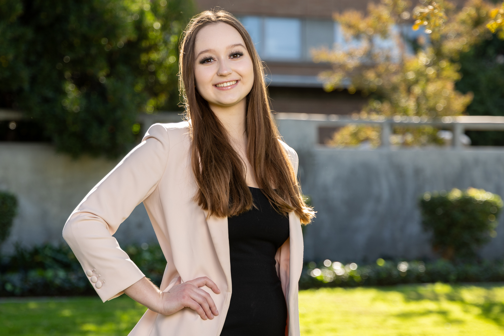 UCR student, Kamilla Minkina, is an art (studio) and art history major, expected to graduate in 2025. She poses on campus by Hinderaker Hall wearing a cream colored blazer and a black dress.