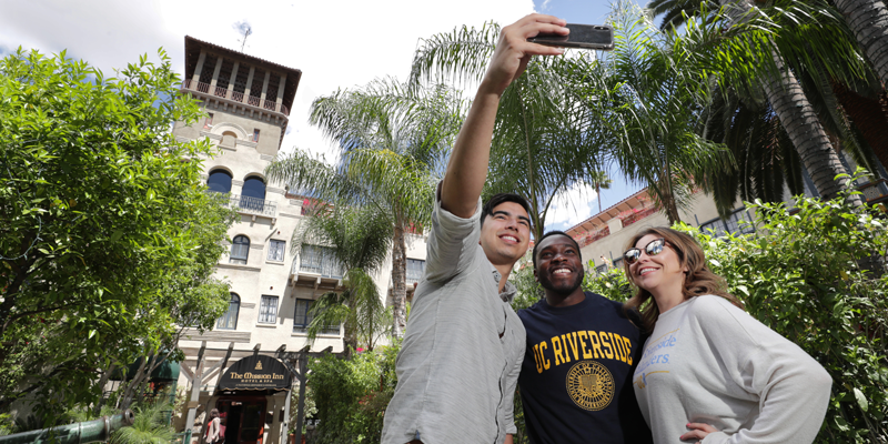 Three students from UC Riverside bunch together to take a selfie outside the Mission Inn in downtown Riverside, Calif.
