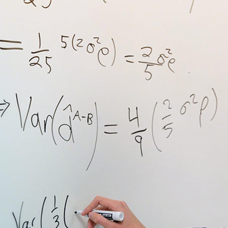 Student works through equations on a whiteboard with professor.