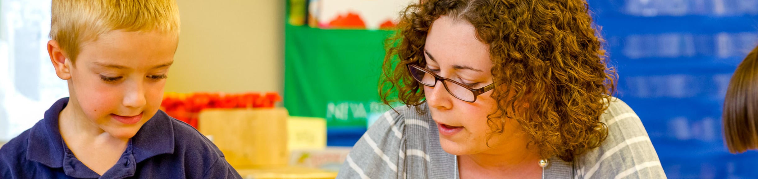 A woman works with a young boy in a classroom setting.