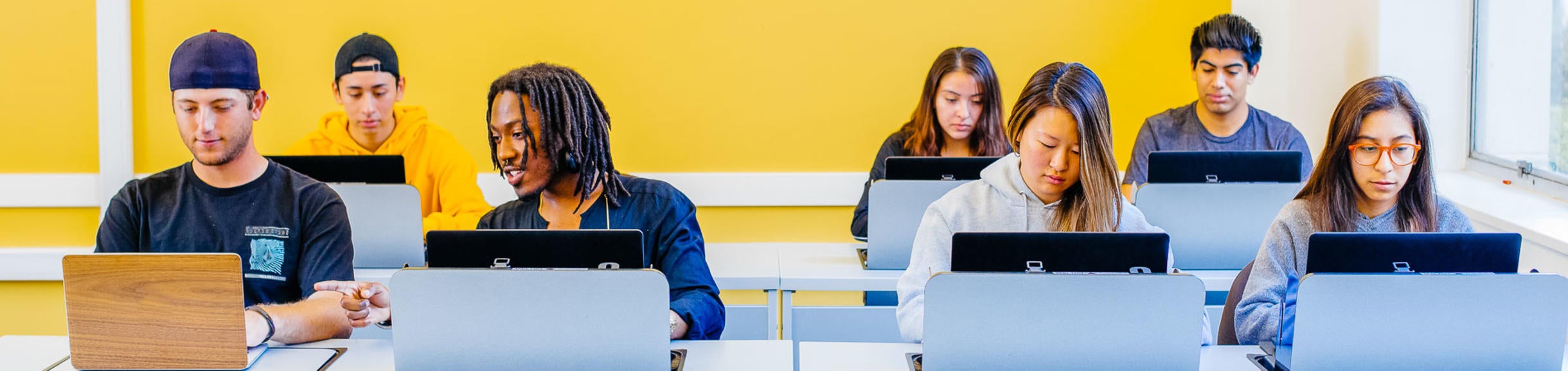 A diverse group of students sitting in a classroom and using laptops to study.