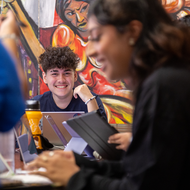 A male student smiles as he sits with his laptop and chats with other students inside Chicano Student Programs' office on the UC Riverside campus.