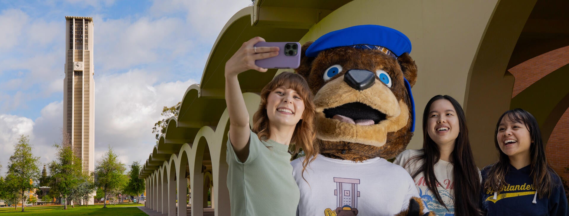 Photo illustration of students posing and taking a selfie with Scotty, UCR's mascot, a bear, in front of the Rivera Library arches and the Bell Tower in the background.