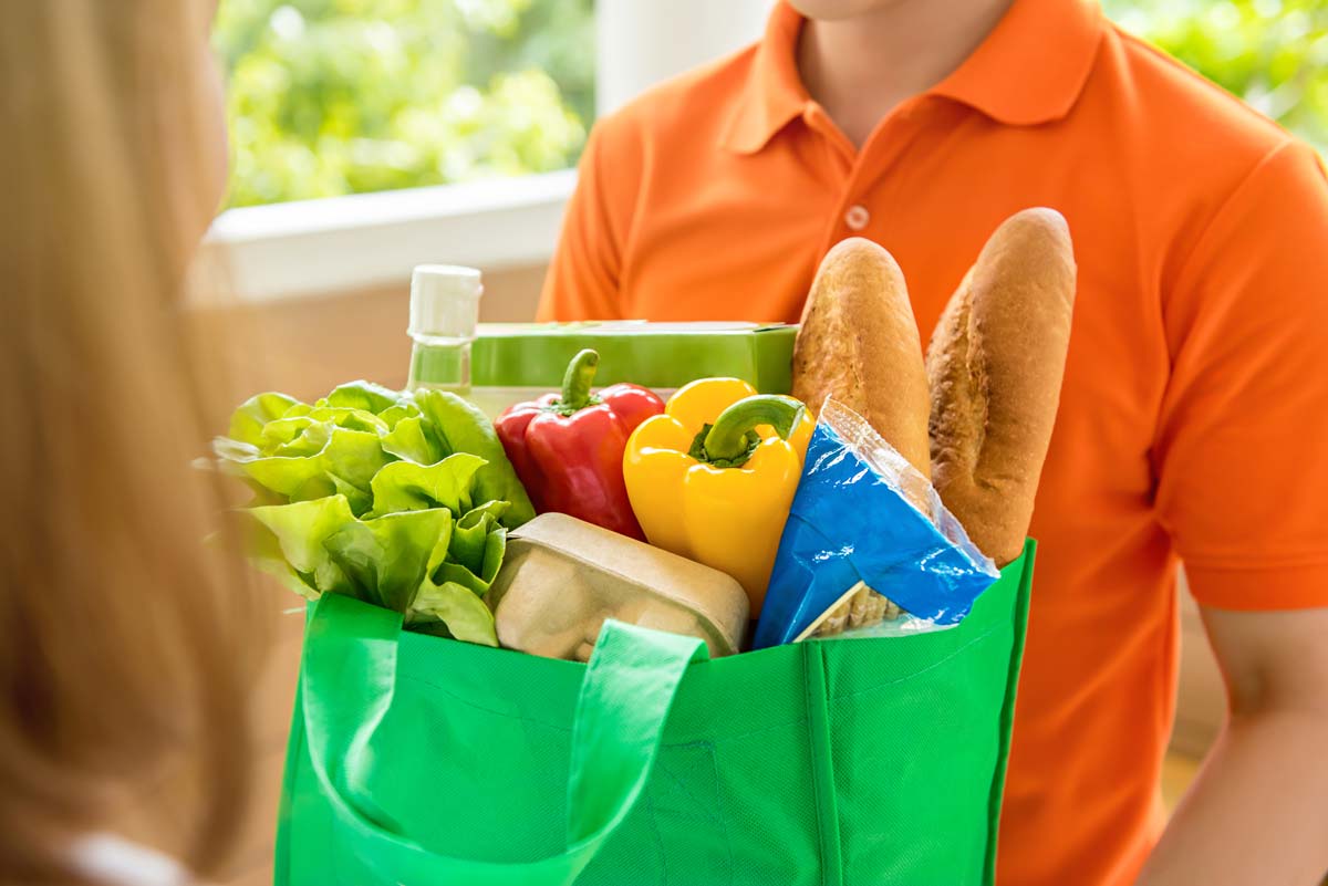 Delivery person holding a reusable bag full of fresh produce and other foods.
