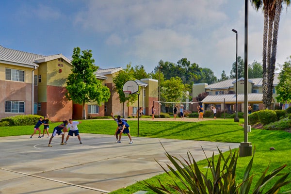 Group of friends playing basketball at a court located at an apartment complex that has park-like scenery.