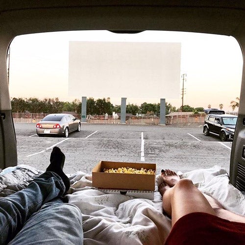 Two UCR students laying in the back of a vehicle looking out a drive-in screen, while enjoying popcorn.