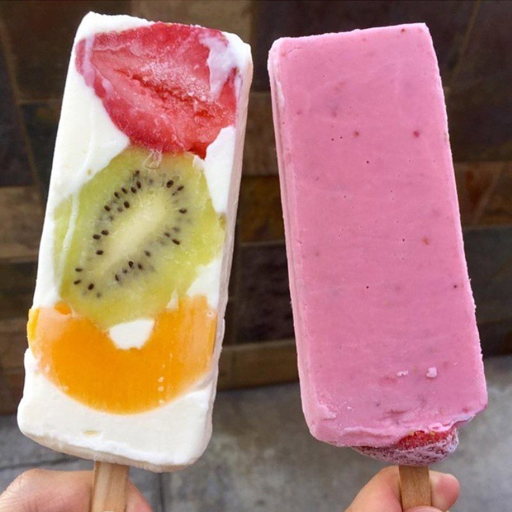Two fruit ice cream bars; one is pink and the other is white with slices of strawberry, kiwi and peach.