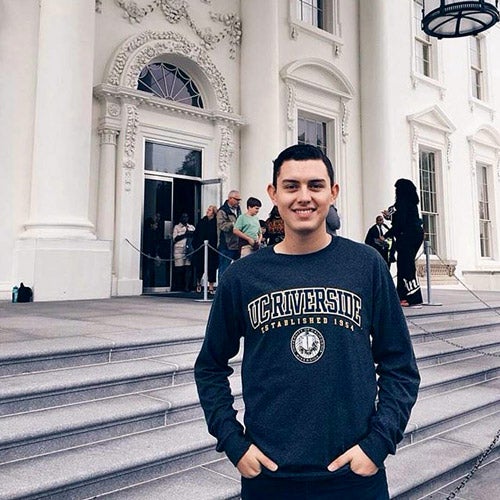 UCR student wearing a UC Riverside shirt, proudly standing in front of historical building.