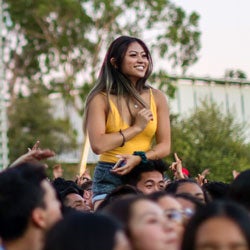 A woman sits on another student's shoulders at a UCR outdoor concert