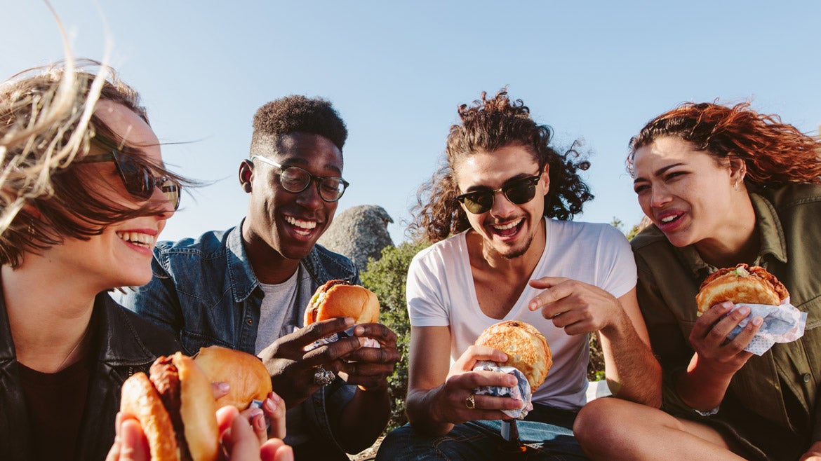 Four smiling students enjoy burgers under a cloudless California sky