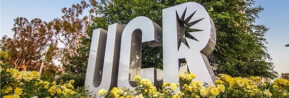 Metal UCR sign surrounded by trees and flowers.