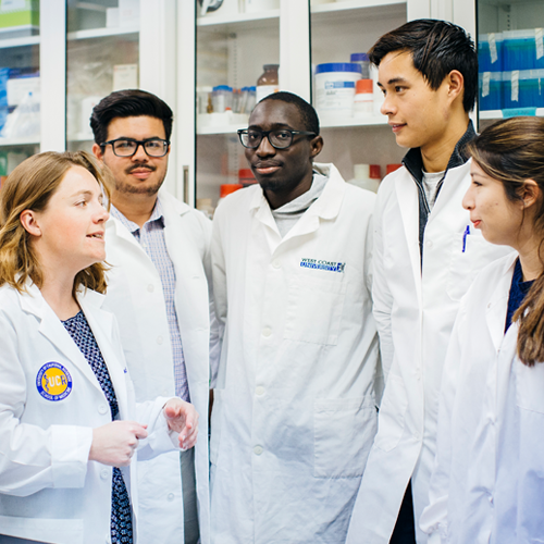 A group of diverse UCR medicine students wearing lab coats gather together in a laboratory. 