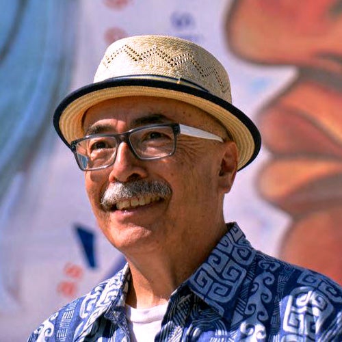 Internationally renowned United States Poet Laureate, Juan Felipe Herrera, smiles in front of a colorful mural painting.