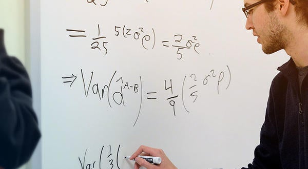 Student works through equations on a whiteboard with professor.