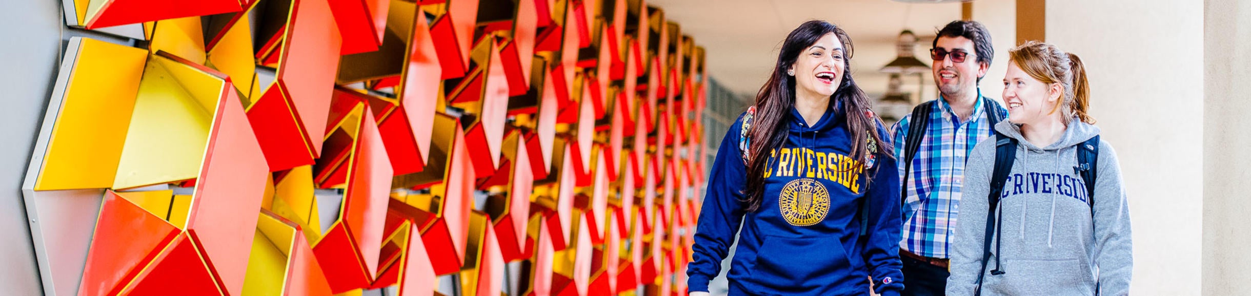 Three students walk by a modern wall sculpture on the UC Riverside campus