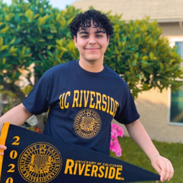 Smiling male student wearing a UC Riverside t-shirt and holding a UC Riverside Pennant